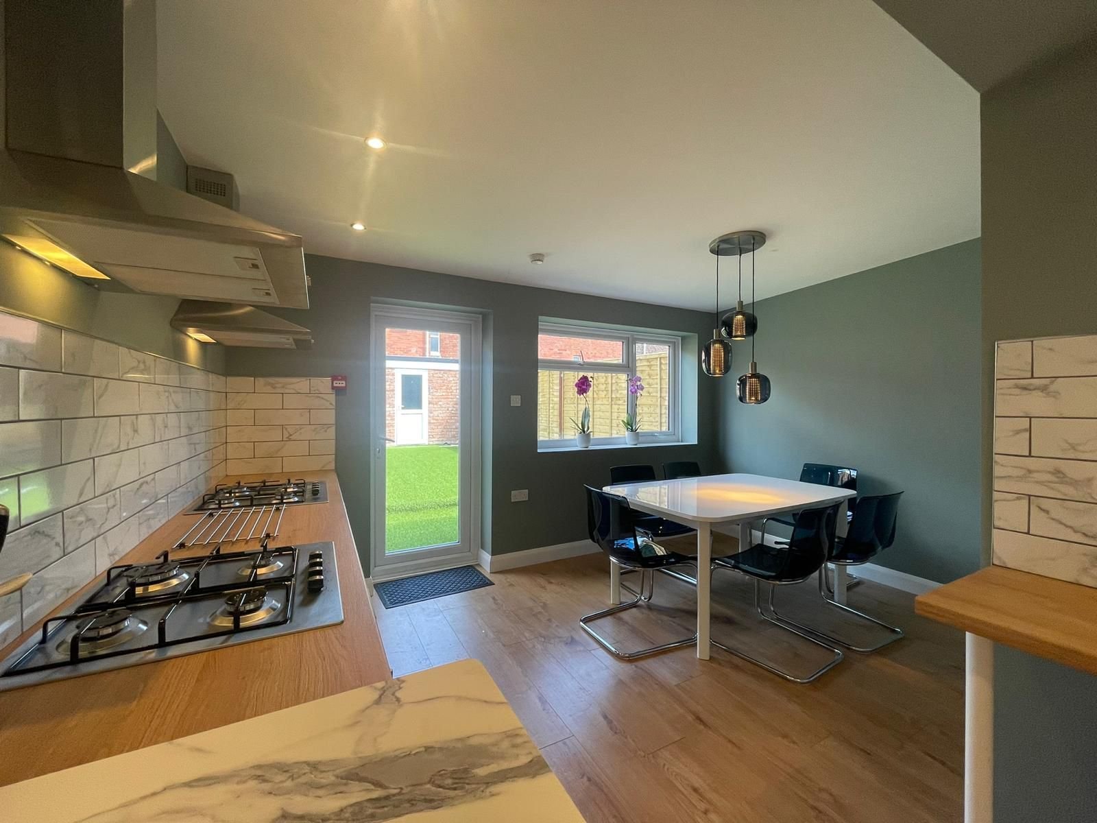 Open-concept kitchen and living room with granite counters, wooden furniture, and modern lighting fixtures throughout the space.